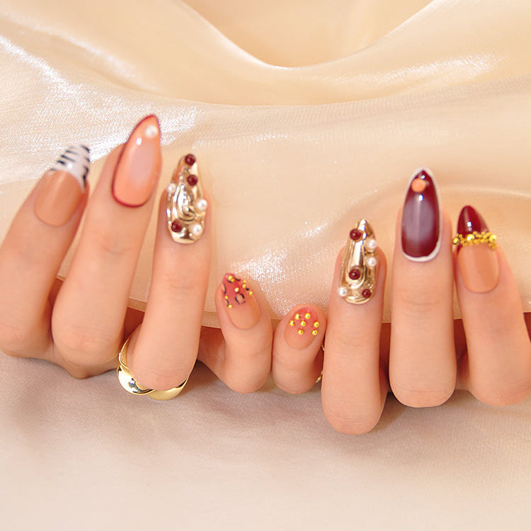 Luxury mixed-media nails with metallic gold texture, pearls, and deep red accents