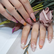 Handmade peach and pink nails with floral designs, pearls, and rhinestones