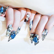 Long stiletto press-on nails featuring metallic silver foil, blue roses, and rhinestone bows