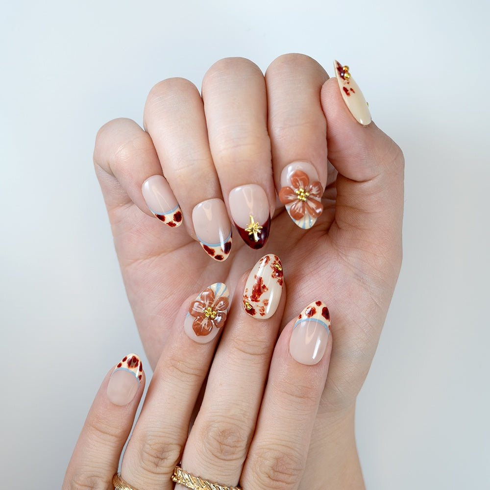 Nude almond nails featuring amber French tips, brown floral patterns and gold studs