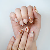 Nude almond nails featuring amber French tips, brown floral patterns and gold studs