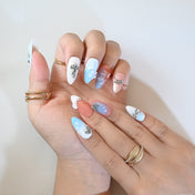 Stylish press-on nails with soft pastel hues, silver metallic charms, and delicate floral patterns