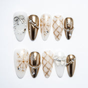 Winter press-on nails with gold snowflake patterns, pearl chains, and metallic bow accents
