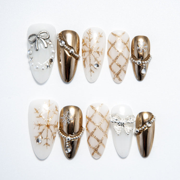 Winter press-on nails with gold snowflake patterns, pearl chains, and metallic bow accents