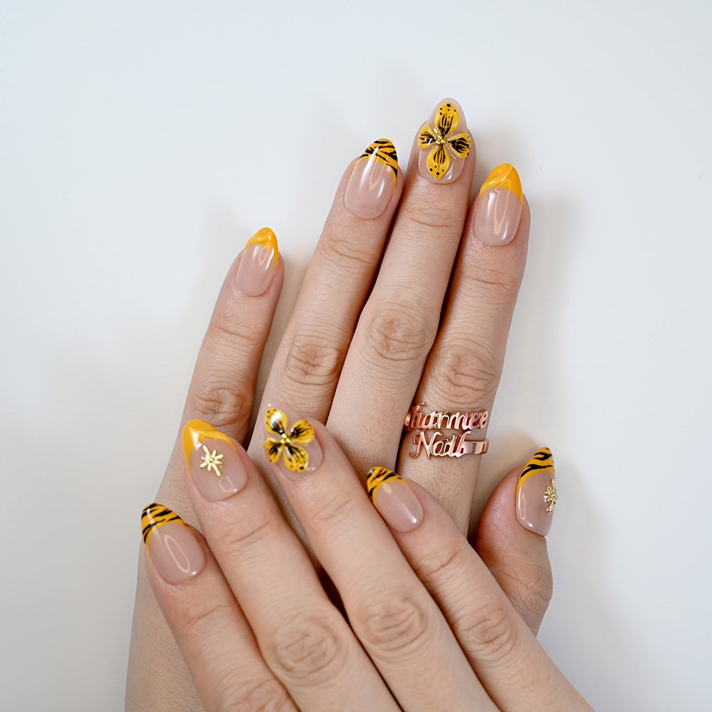Luxury yellow French tip nails with black tiger stripes and gold embellishments