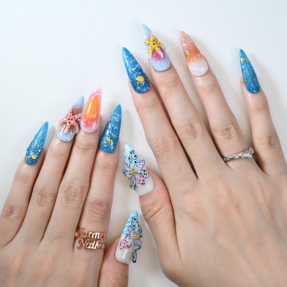 Beach-inspired acrylic nails featuring blue glitter, sunset gradient, and 3D sea creatures