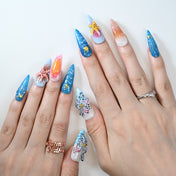 Beach-inspired acrylic nails featuring blue glitter, sunset gradient, and 3D sea creatures