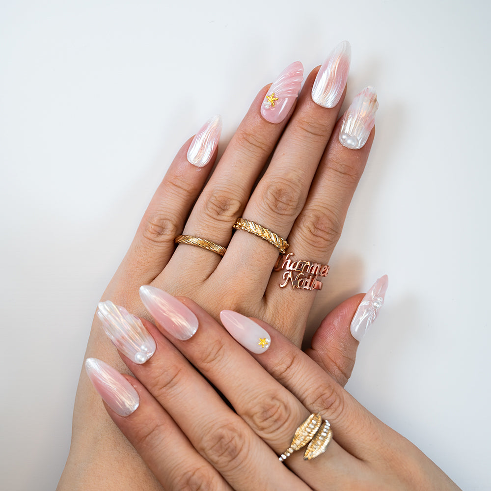 Medium almond nails with pearlescent shine, seashell carvings and tiny gold stars