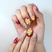 Trendy long floral press-on nails with red tips, pearls, and multicolor gemstone designs
