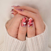 Festive holiday nails with glittery nude base, red gift wrap art, and decorative beads