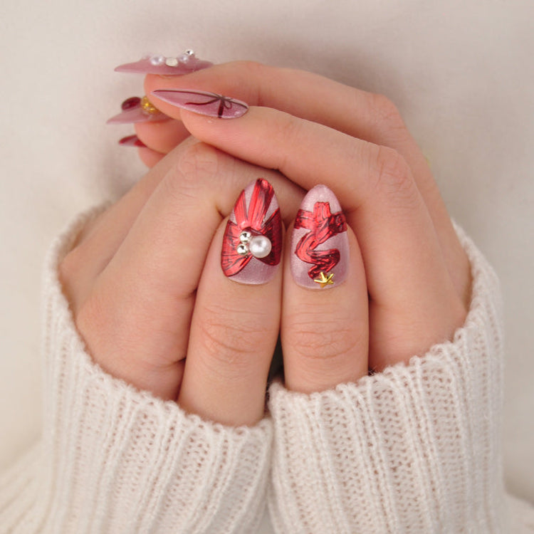 Festive holiday nails with glittery nude base, red gift wrap art, and decorative beads