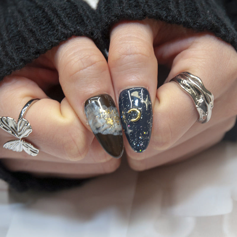 Almond-shaped black press-on nails featuring cosmic star and moon design
