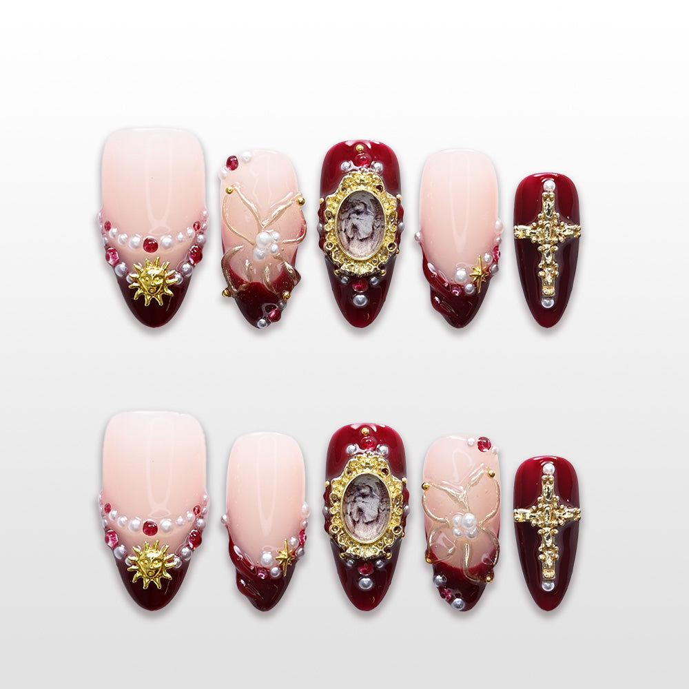 Burgundy press-on nails with pearls, gold cross charms, and vintage frame accents