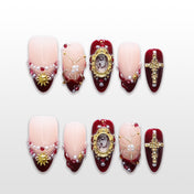 Burgundy press-on nails with pearls, gold cross charms, and vintage frame accents