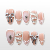 Nude pink press-on nails with silver bow, pearl beads, and French tips