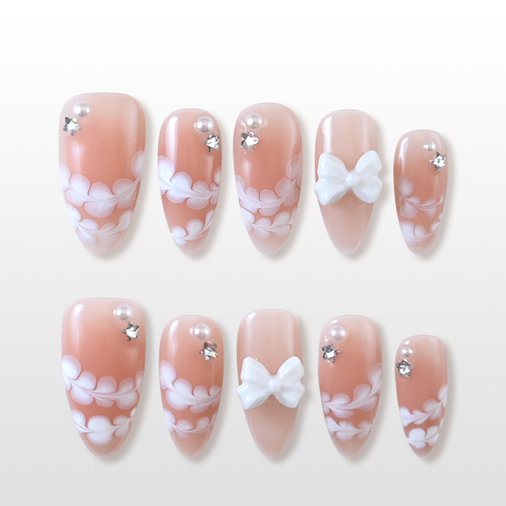 Nude pink press-on nails with white floral lace and 3D bow accents