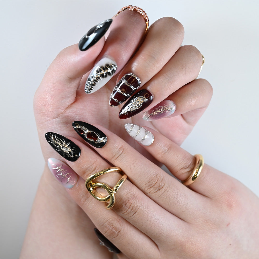 Hand model wearing punk-inspired press on nails with gold threads, chrome chains, and crystal gems