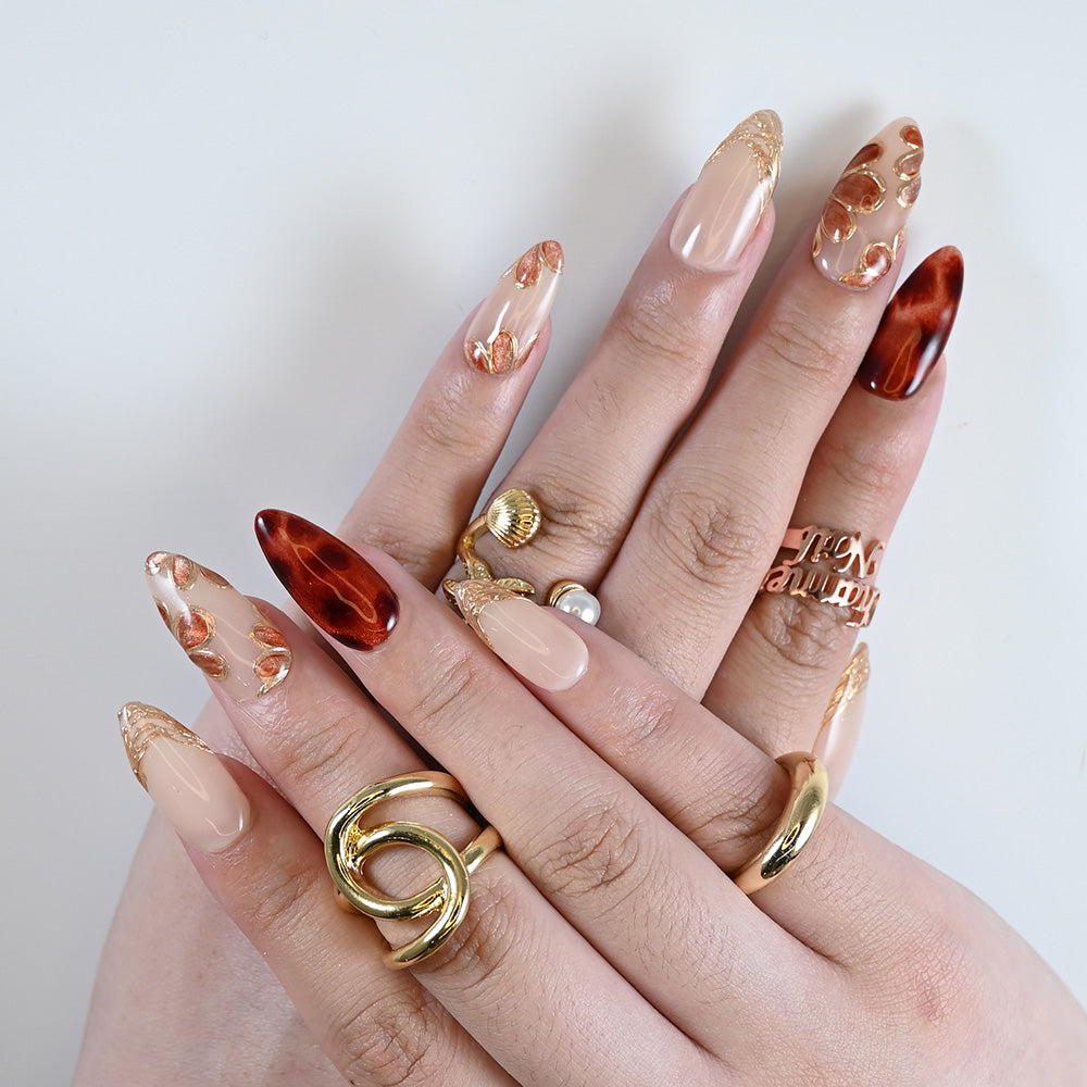  Nude almond shaped nails featuring glossy amber patterns and golden carved tips