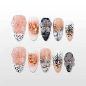 Nude and white press-on nails with 3D floral accents, gold petals, and black polka dots