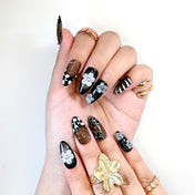 Handmade press-on nails with metallic gold, monochrome floral patterns, and stripe details