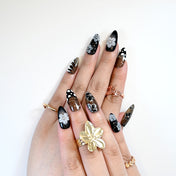 Chic black and gold floral nails with 3D art, glitter details, and stripe patterns
