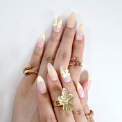 Handmade almond nails with soft ombre pink-yellow tips, pearls, and bow charm