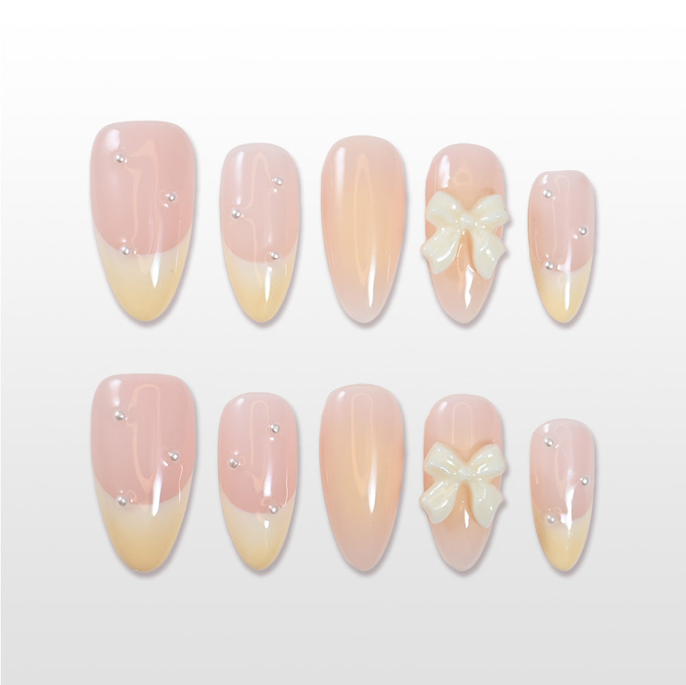 Pastel pink and yellow gradient press-on nails with 3D bow accent and pearl details