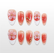 Medium almond press-on nails with coral pink gradient, 3D pink flowers, and gold accents