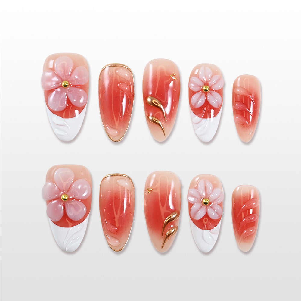 Medium almond press-on nails with coral pink gradient, 3D pink flowers, and gold accents