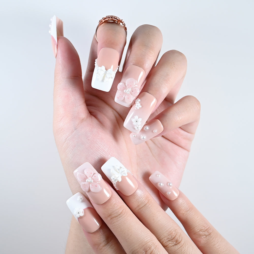 Handmade nude pink nails with floral accents and white lace-up design