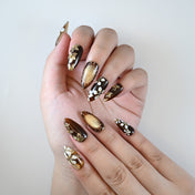 Medium almond reusable press-on nails in glossy black with gold foil and flower accents