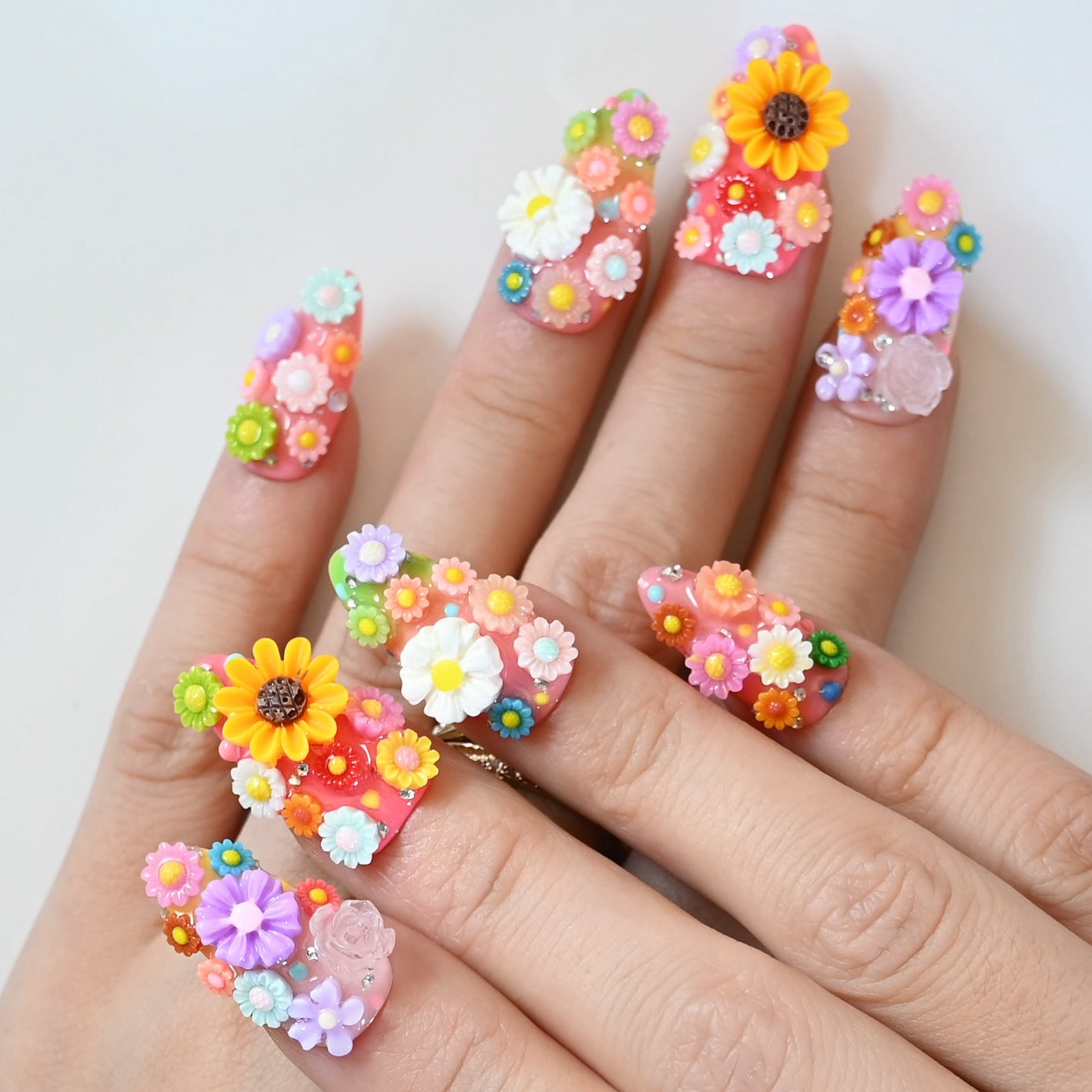 Bright pink press-on nails with 3D flowers, greenery, and sparkling accents