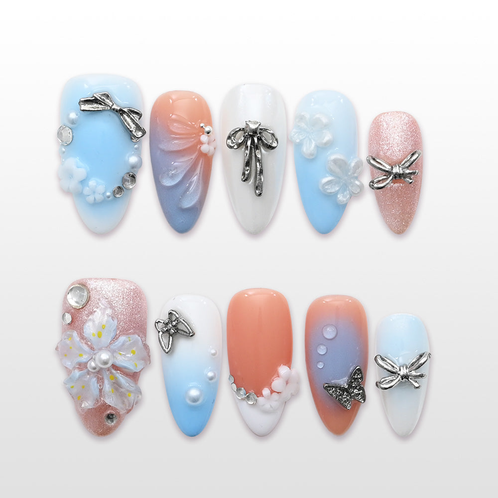 Romantic press-on nails with pastel blue and peach gradient, silver bow charms, and floral accents