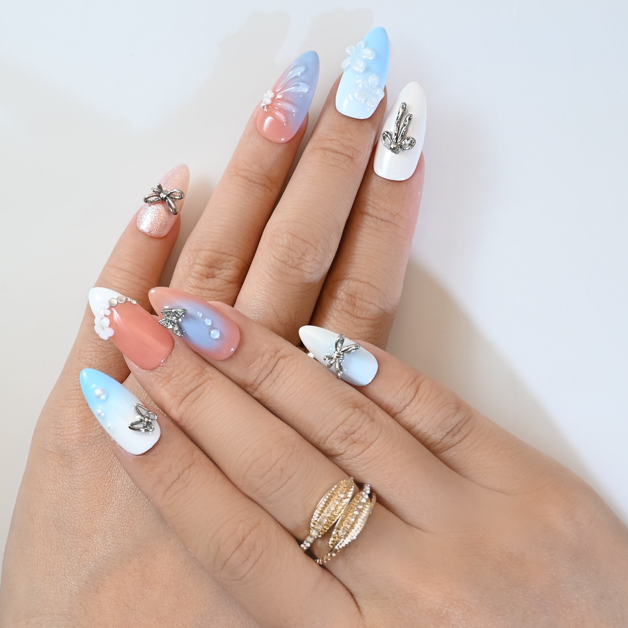 Chic almond press-on nails with coral and blue ombre, pearl details, and crystal bow designs
