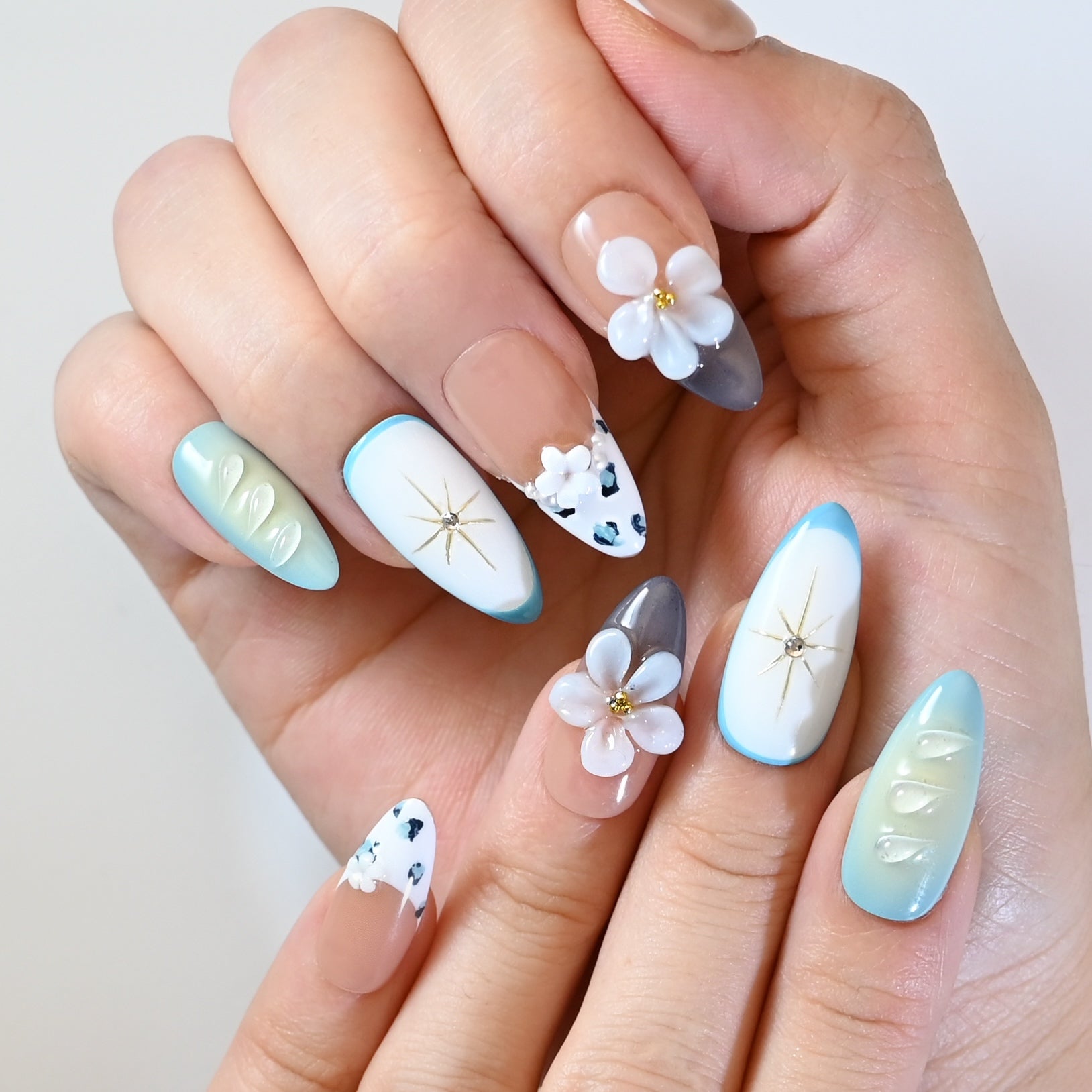 Luxury almond press-on nails with pastel blue tips, gold starburst design, and rhinestone details