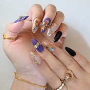 Glam purple and gold press-on nails with bold flower art, rhinestones, and shimmer finish