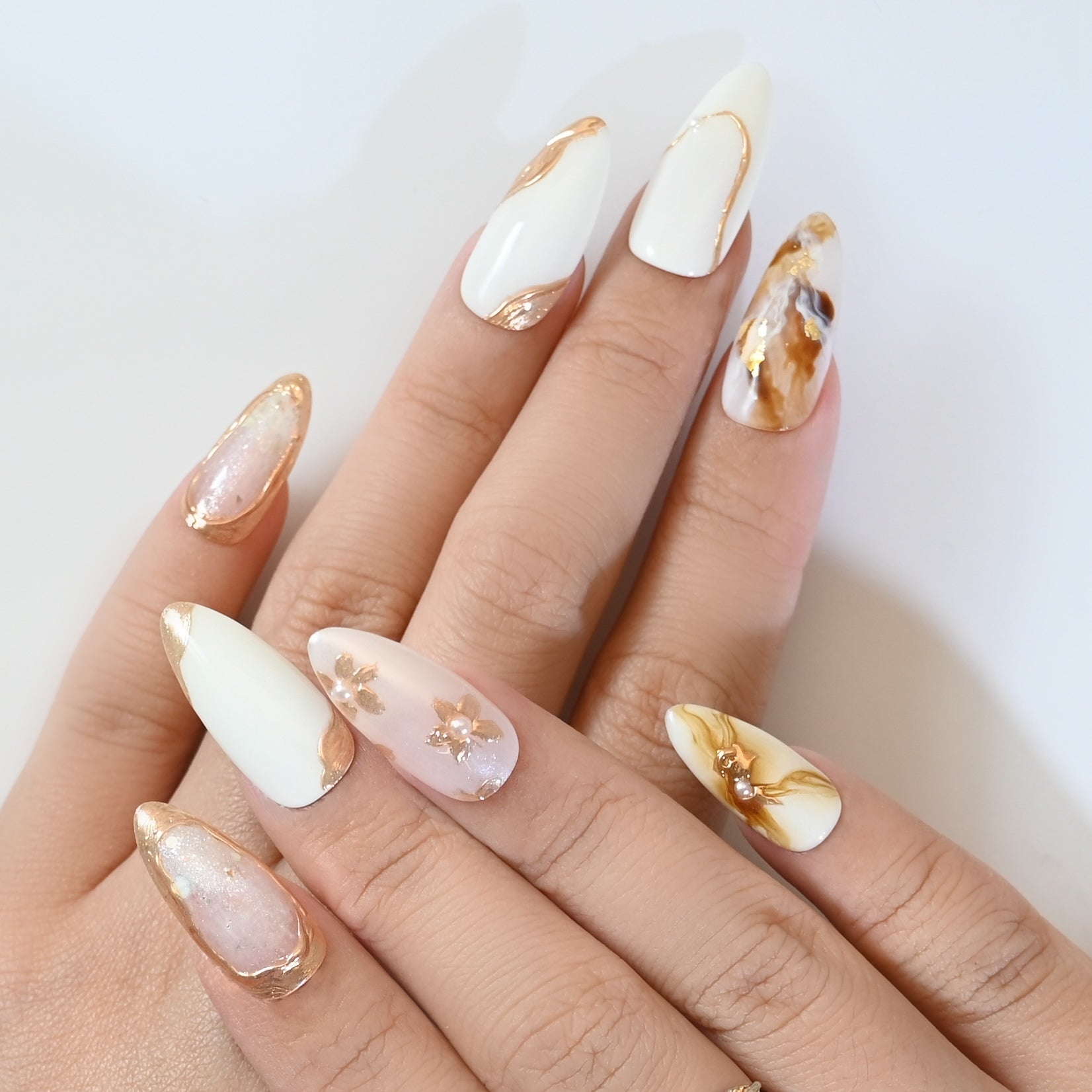 Elegant almond press-on nails in ivory and gold with marble swirl and flower design