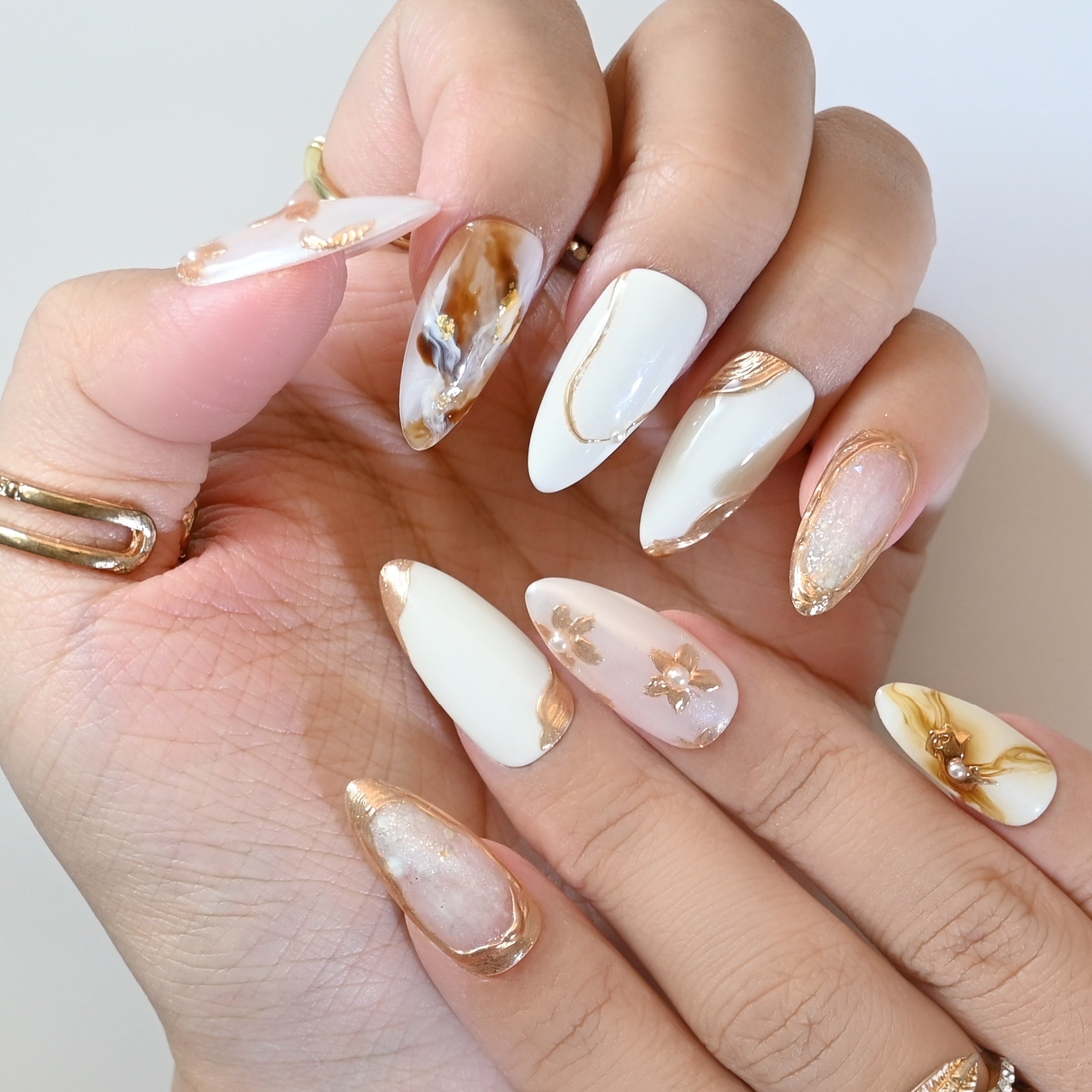 Classy marble and floral press-on nails with gold accents, pearl charms, and glossy finish