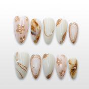 White and gold press-on nails with marble accents, 3D pearl details, and floral patterns