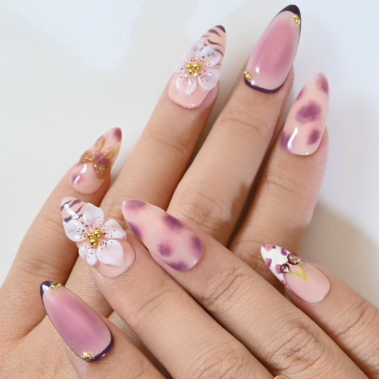 French tip press-on nails in purple leopard pattern with 3D flowers, gold studs, and cherries