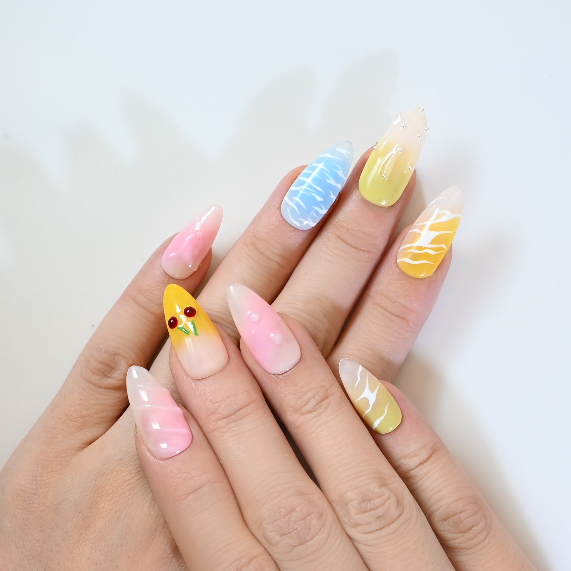 Cute pastel press-on nails with sky blue swirls, cherries, and pink ombre