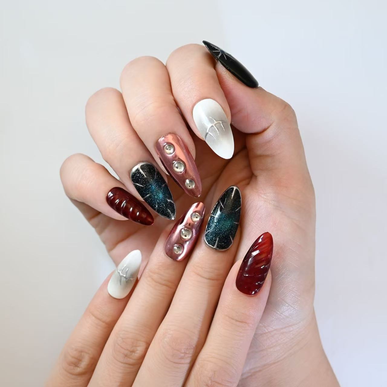 Futuristic press-on nails with metallic red chrome, black galaxy sparkle, and gemstone studs
