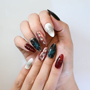 Futuristic press-on nails with metallic red chrome, black galaxy sparkle, and gemstone studs