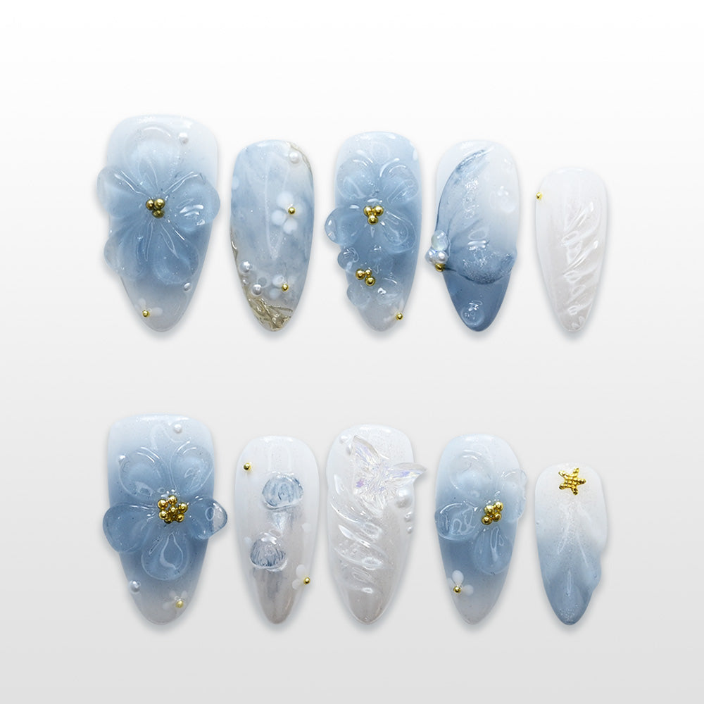 Light blue press-on nails with 3D floral designs, pearl accents, and gold beads