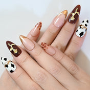 Mixed design press-on nails with cow spots, burgundy base, gold flower charm, and chic style