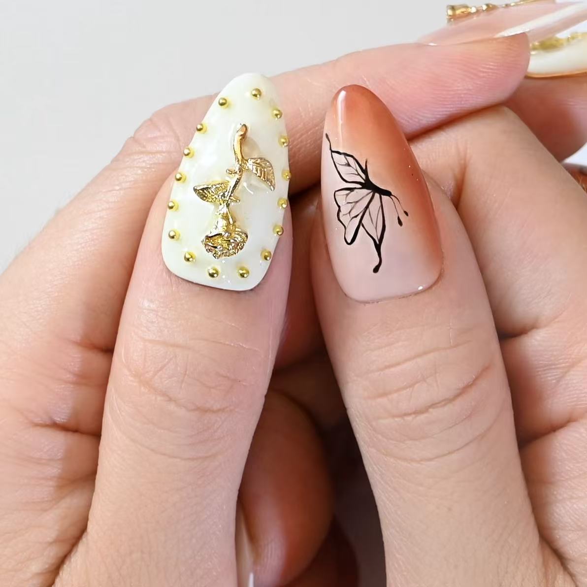 Nude orange press-on nails with gold rose charms, butterfly art, and metallic wave texture