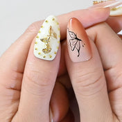 Nude orange press-on nails with gold rose charms, butterfly art, and metallic wave texture