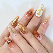Chic peach nude press-on nails with gold metallic art, rose embellishments, and bow details