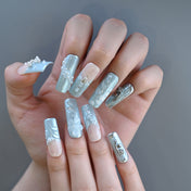 Glamorous blue and silver press-on nails with pearl beading, metal charms, and textured art