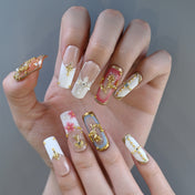 Baroque style press-on nails with gold frame, cross, and gemstone accents